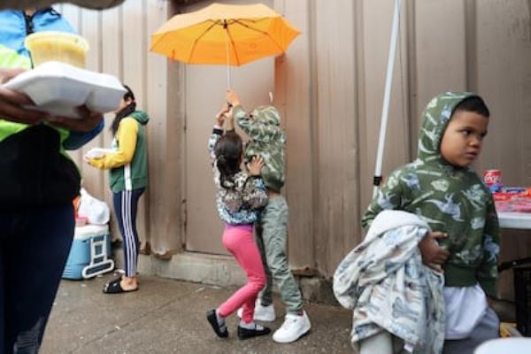 Dos niños juegan mientras su madre lleva co<em></em>ntenedores de comida fuera de un refugio para inmigrantes en South Halsted Street (Chicago), en abril de 2024.