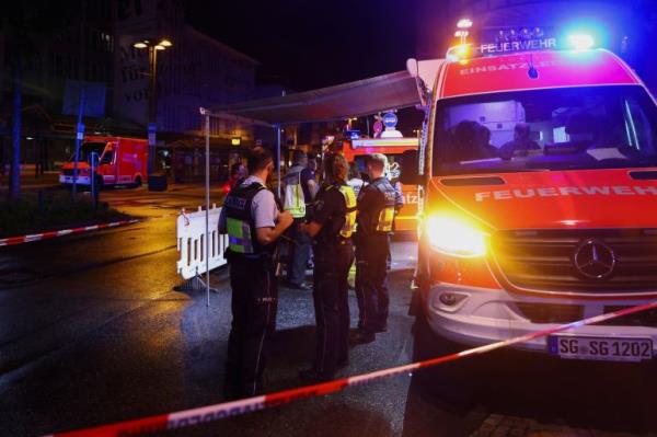 Police vehicles with lights blazing illuminate an area cordo<em></em>ned off by crime-scene tape, wher<em></em>e officers look around.
