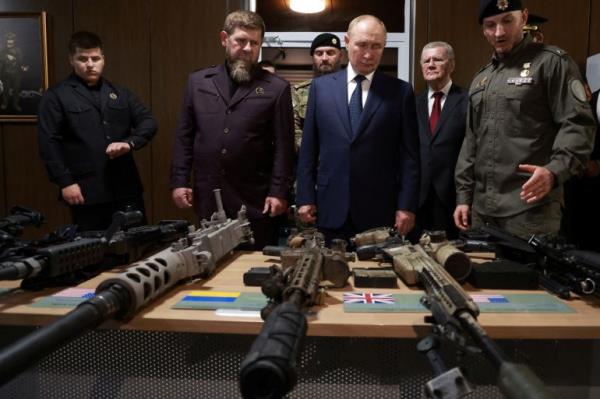 Putin and Kadyrov looking at weapons. The guns are laid out on a table in front of them. Another man is speaking to Putin
