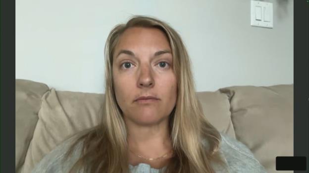 Blo<em></em>nde woman in grey shirt sitting on a beige couch