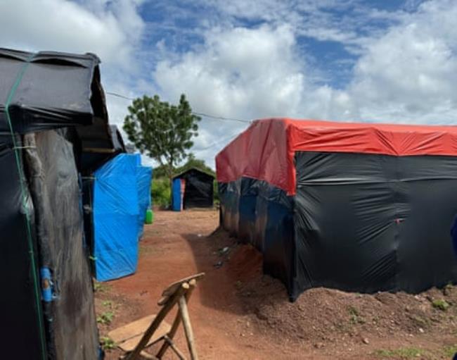 Makeshift tents made out of black nylon stretched over poles in a rural setting