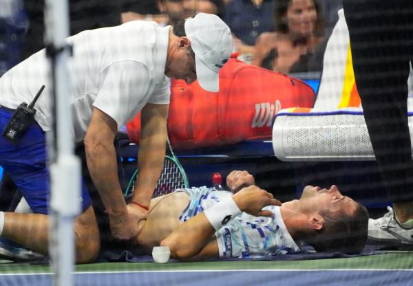 Laslo Djere, who was suffering an abdominal injury, is tended to by a trainer during his second-round loss to Novak Djokovic at the U.S. Open.