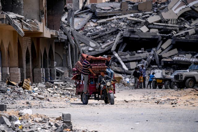 A three-wheel vehicle carries belo<em></em>ngings away from destroyed buildings