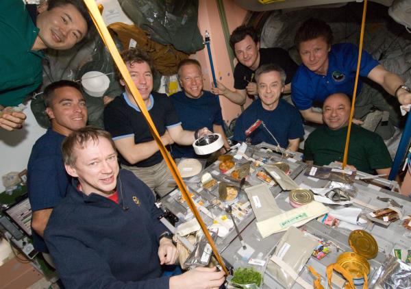 Nine of the 13 Expedition 20 and STS-127 crew members share a meal, as NASA astro<em></em>naut Michael R. Barratt holds the Apollo 11 Moon rock