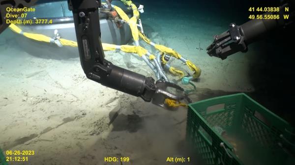The clip shows a remotely operated vehicle attaching ropes and equipment to what appears to be the end cap of the sunken vessel. 