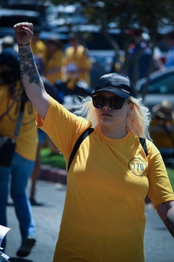 A young woman in a yellow shirt raises her fist.