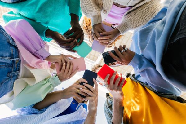 A low-angle view of six people from diverse racial backgrounds holding cellphones.