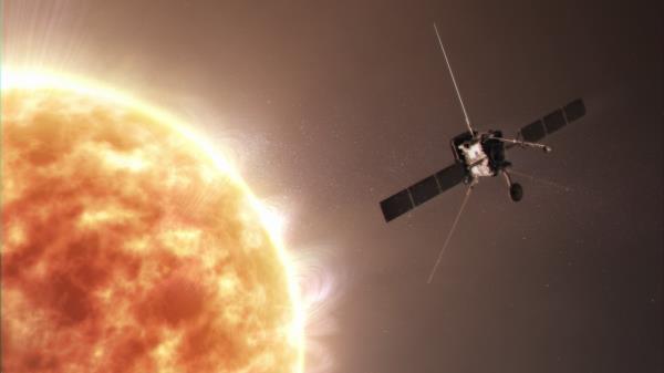 A portion of the Sun fills most of the left side of the image. On the right against the backdro<em></em>p of space is Solar Orbiter with two long, black solar panels protruding from each side of the silver, box-shaped spacecraft and thin radio antennas attached to the top, back, bottom left, and bottom right of the spacecraft.