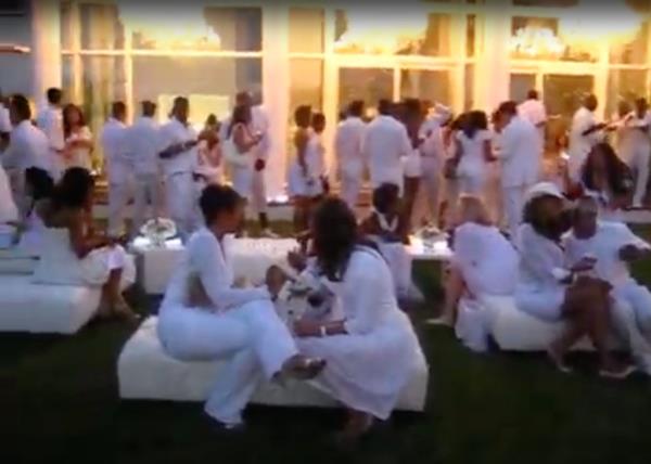 Sean Love Combs, also known as Diddy, with a group of guests in white outfits sitting on a white couch at one of his White Parties in the Hamptons