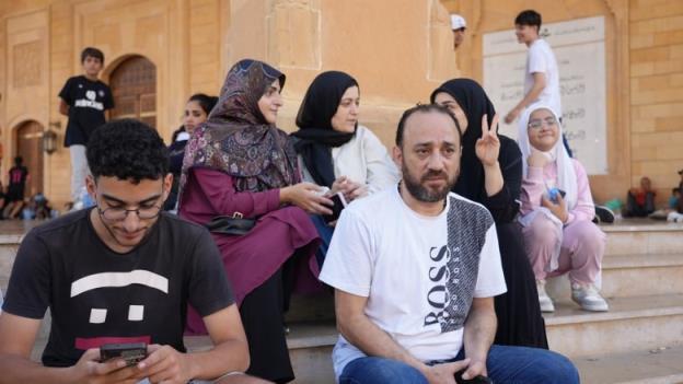 A man and his family sit on steps outside a mosque.
