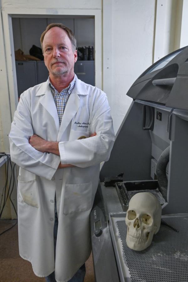 Photo shows Dr. Bradley Adams in a lab coat next to a recreated skull.