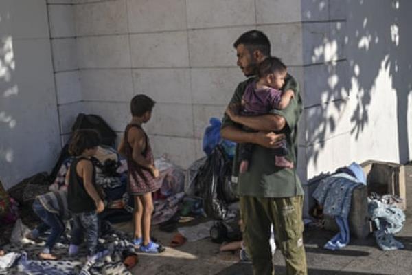A man holding a young child looks back at two more children and their belongings