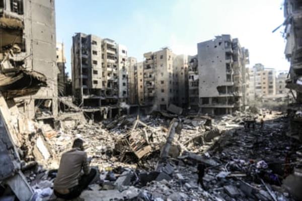 A man crouches overlooking the rubble of several razed buildings