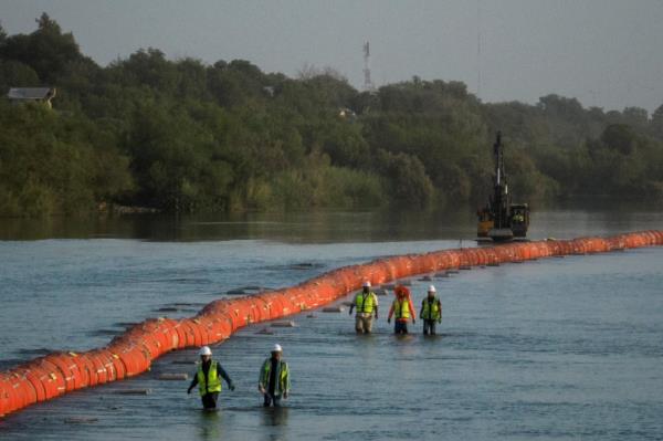 Workers wade past buoys placed in the Rio Grande river by Texas Gov. Greg Abbott as part of his border security effort.
