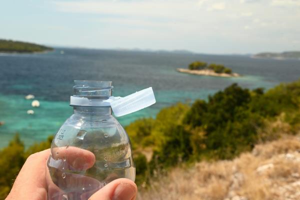A plastic bottle with a tethered cap and the sea in the background.