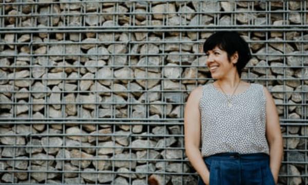Woman leaning against stones behind metal cage