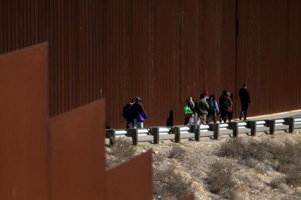 A group of migrants walk to an open gate on the US-Mexico border wall to be processed by the border patrol after illegally crossing into the USA from Tijuana on Nov. 11, 2022.