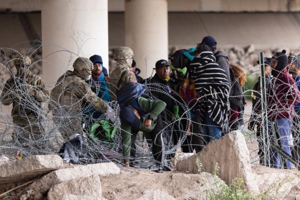 A large group of almost 60 migrants are co<em></em>nfronted by Texas Natio<em></em>nal Guard after they illegally crossed the border and breached wire barriers near the Rio Grande on March 26, 2024.