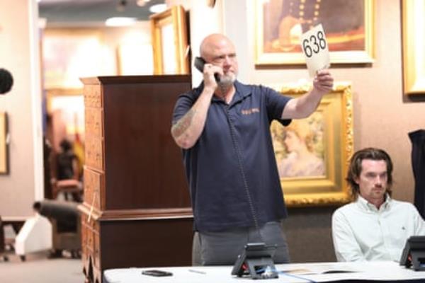 A person holds the number 638 while waiting tersely on the phone in an auction house