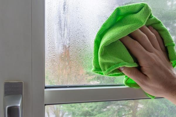 A hand cleaning window with green microfiber cloth