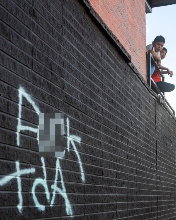 Two boys stand on an apartment balcony in Aurora, Colorado, wher<em></em>e anti TdA graffiti is painted.