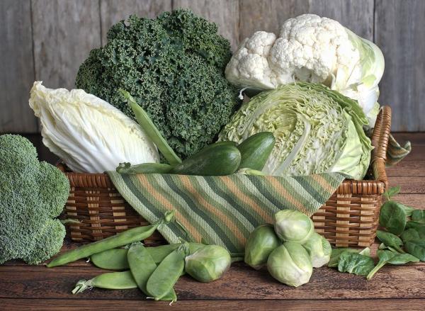 Mixed green vegetables in a basket on a wooden table