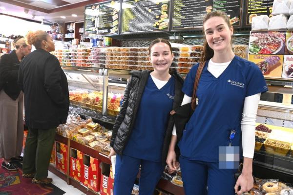 Two nursing students, Katie Mcgeehan and Zoe Carty, seen posing in scrubs in front of deli display.