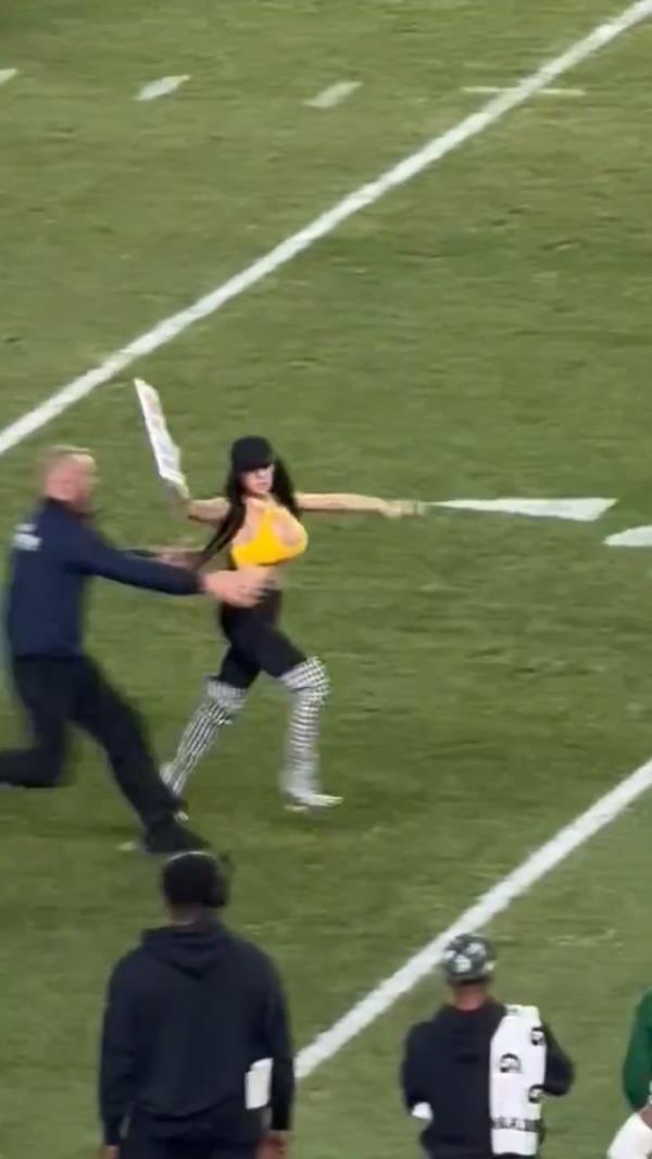 Woman running o<em></em>nto a football field with a pro-Trump sign during the Steelers and Jets game