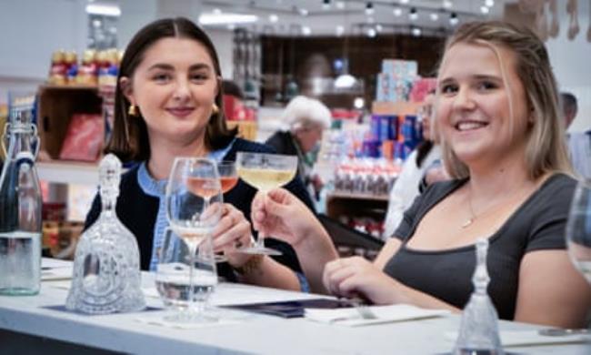 Two young women smiling and cl<em></em>inking glasses at the champagne bar