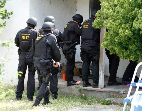 Five heavily armored California Bureau of Narcotics Enforcement Officers at a doorway.