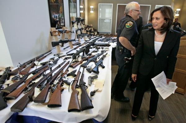 Kamala looking over a table of guns 