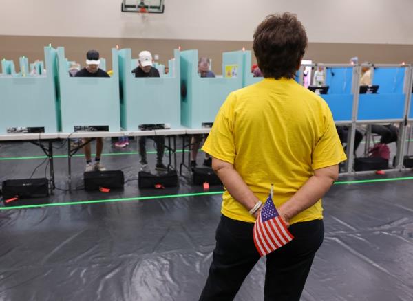 Clark County Election Department volunteer, wearing a yellow shirt, holding an American flag while assisting voters during early voting in Las Vegas, Nevada
